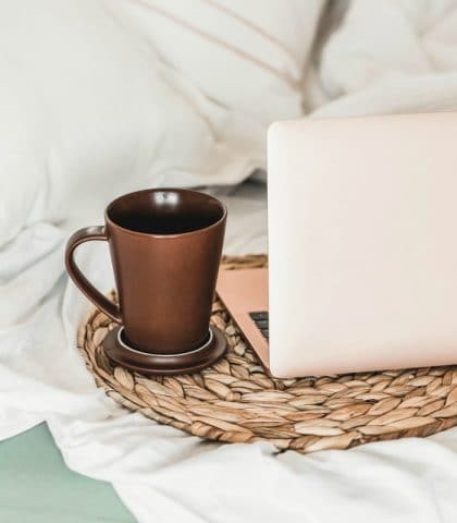 IG trust score, Rose colored laptop on bed with woven placemat and brown coffee cup.