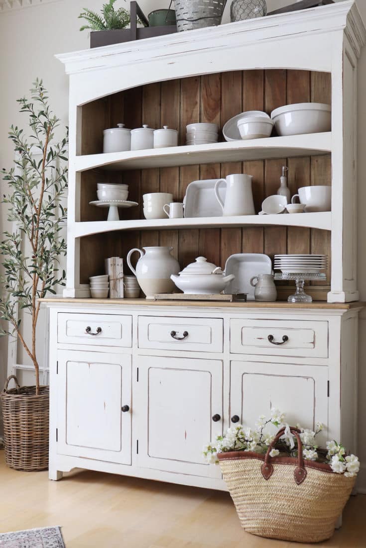 white farmhouse buffet and hutch filled with white pottery with olive tree and market basket
