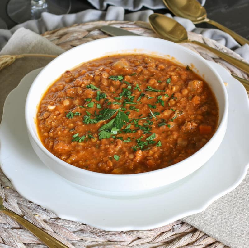 Hearty and healthy brown lentil soup served in white bowl with gold utensils