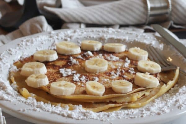 plated stack of homemade crepes with bananas and powdered sugar