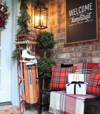 Christmas front porch decor with vintage sled and plaid pillows and blankets on a bench to welcome friends