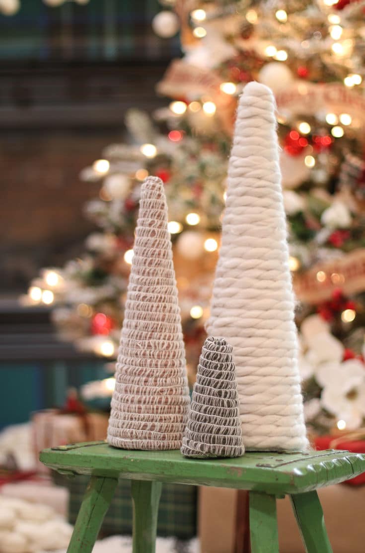 two different size and different color mambo mini Christmas trees and one large thick yarn tree in front of Christmas lights