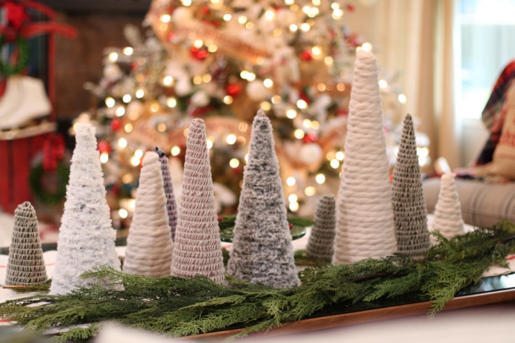 Mini Christmas trees in different sizes made from different types of yarn with lights of Christmas tree behind