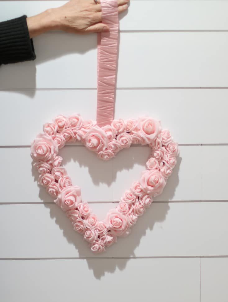 pink heart shaped Valentines Day wreath made from pink foam roses with crushed satin pink ribbon against white shiplap wall
