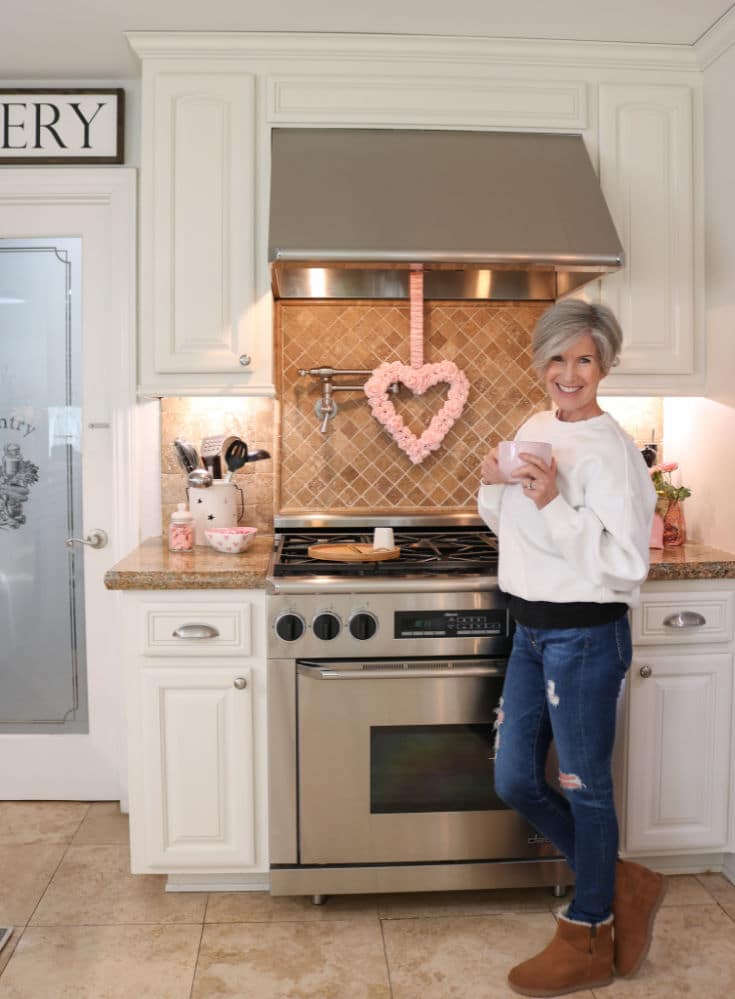 Woman posing in white kitchen next to stainless steel stove decorated with Valentines Day wreath